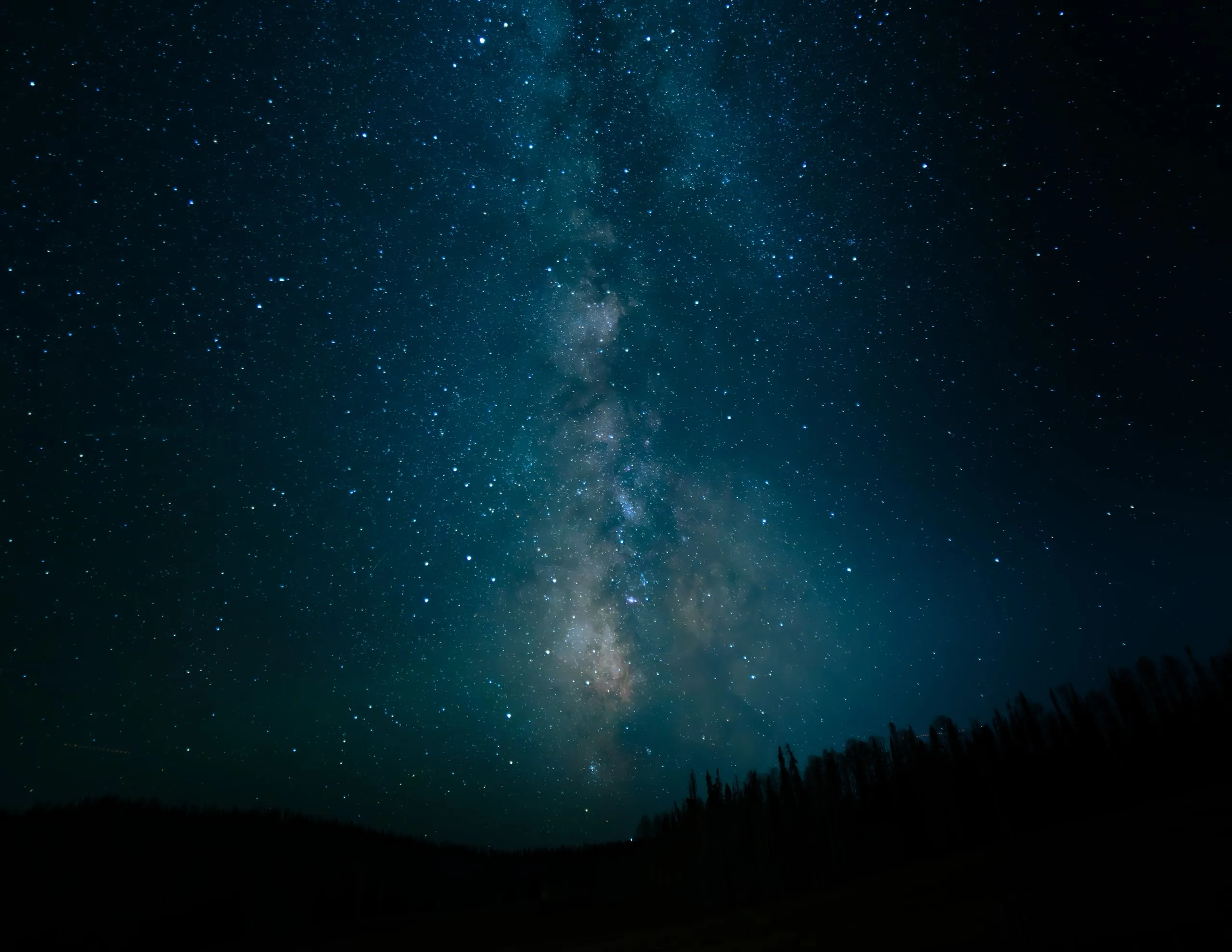 The Milky Way's bright core rising over a dark silhouetted mountain ridge and treeline