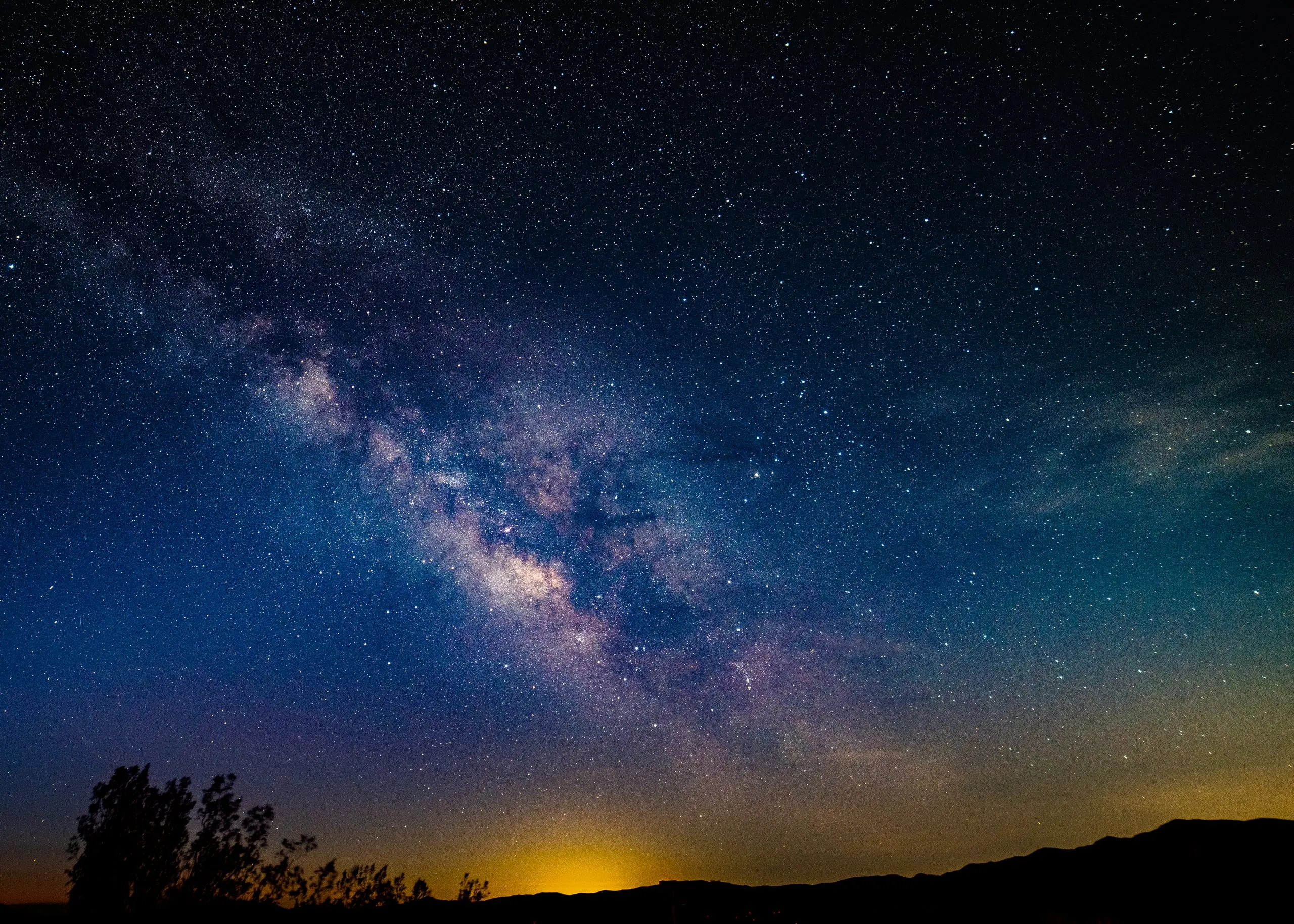 The Milky Way's bright core rising over a dark desert horizon with a faint glow of distant light pollution